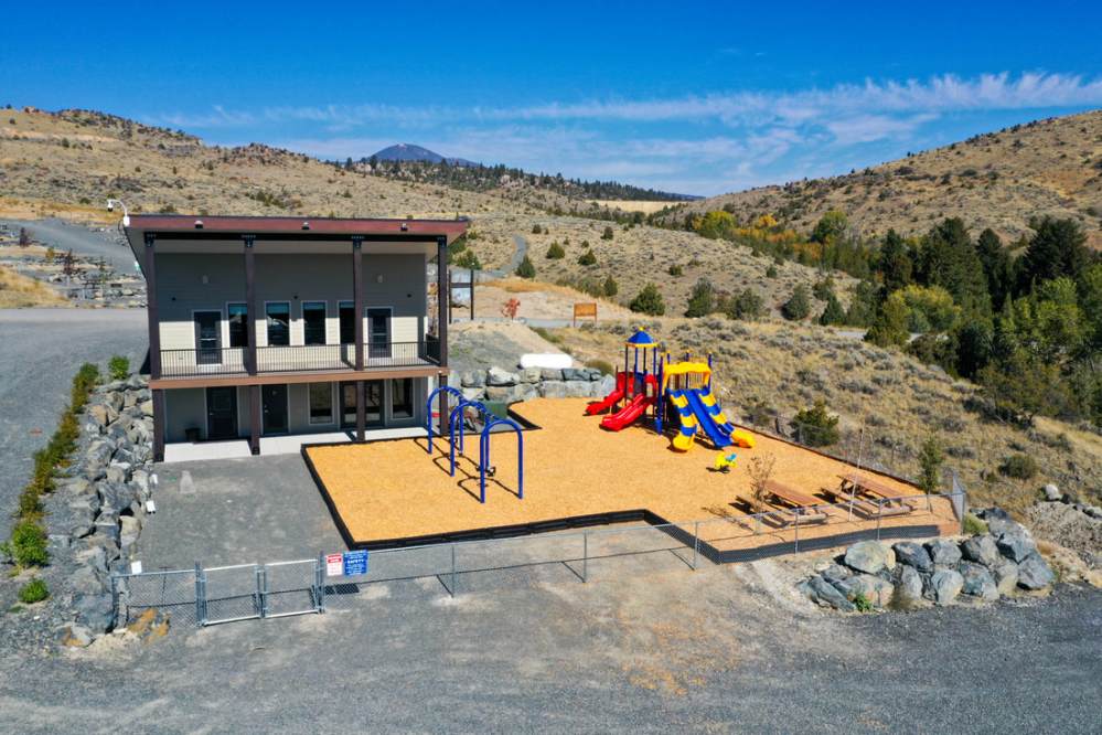 Remote playground with slides and climbing structures near a two-story building in a hilly landscape.